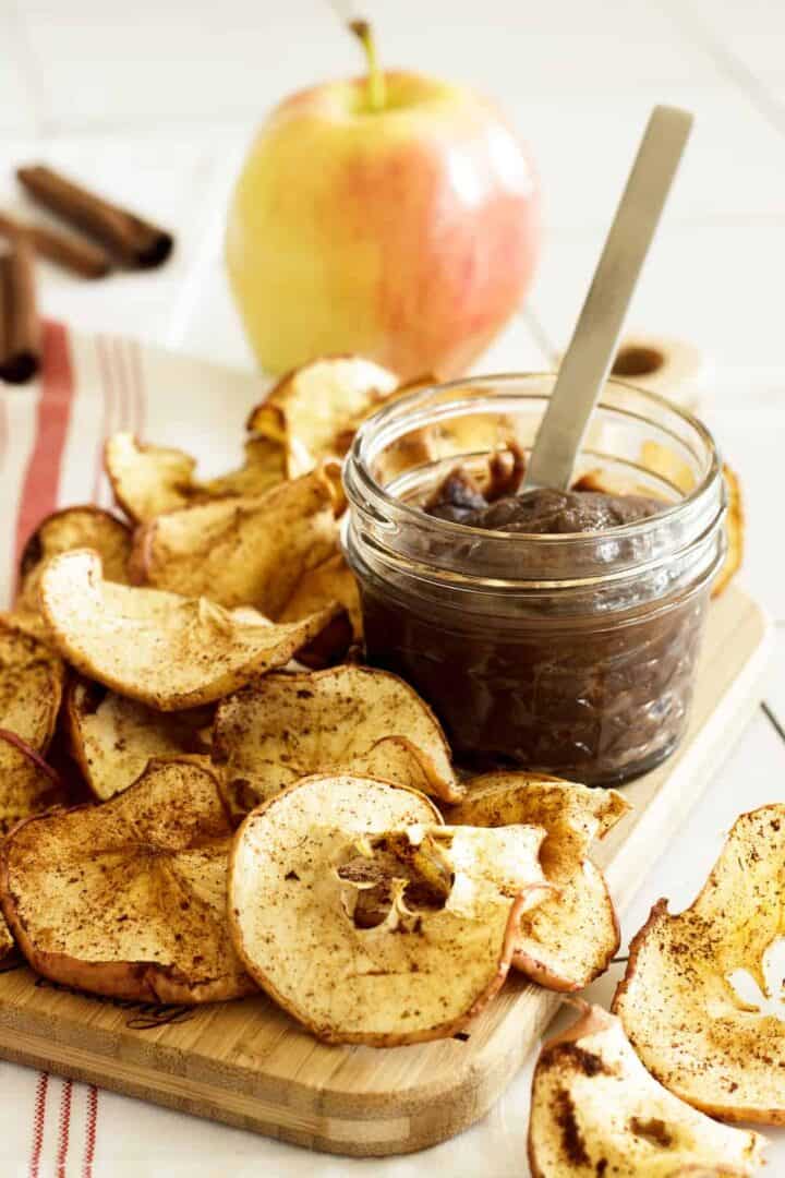 A pile of apple chips next to a jar of chocolate dip.