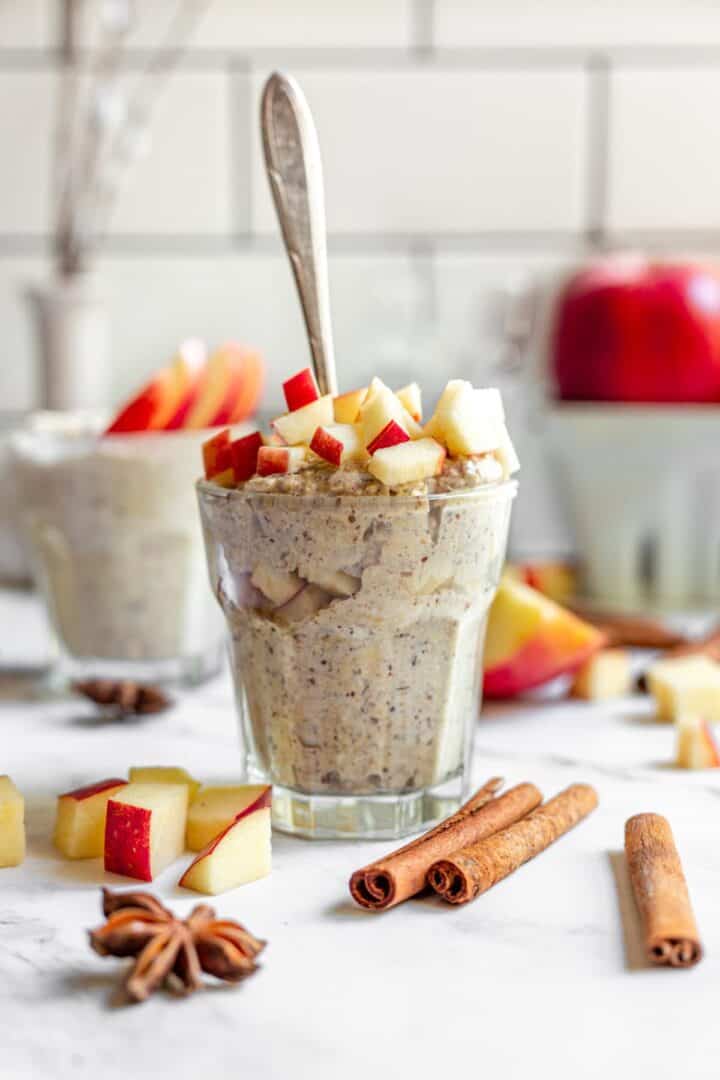 A glass of overnight oats decorated withe diced apples, and whole spices.