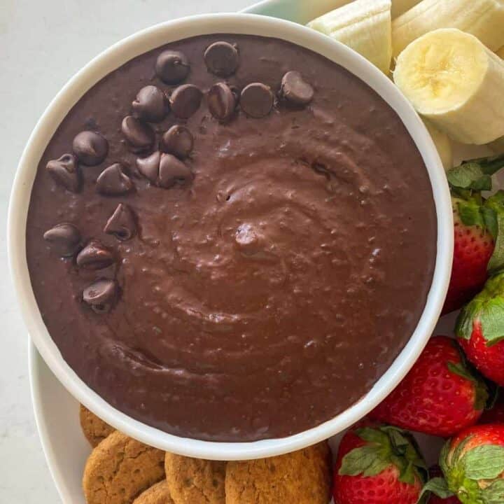A bowl of chocolate hummus next to cookies, strawberries and bananas.