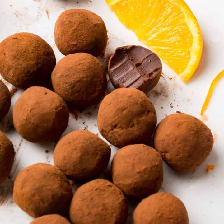 Cocoa powder coated truffles in a white plate next to a slice of orange.