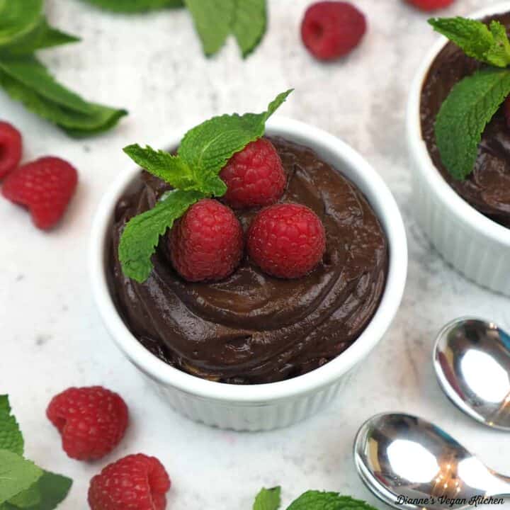 A ramekin full of dark chocolate mousse topped with raspberries and mint.