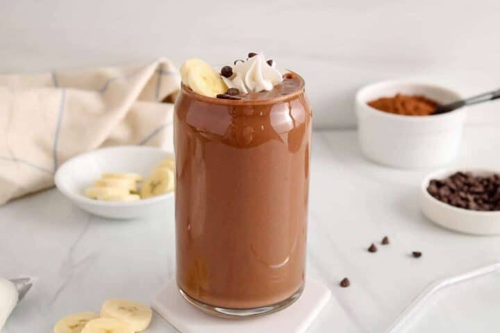 A glass with chocolate milkshake in, topped with bananas, cream and chocolate chips.