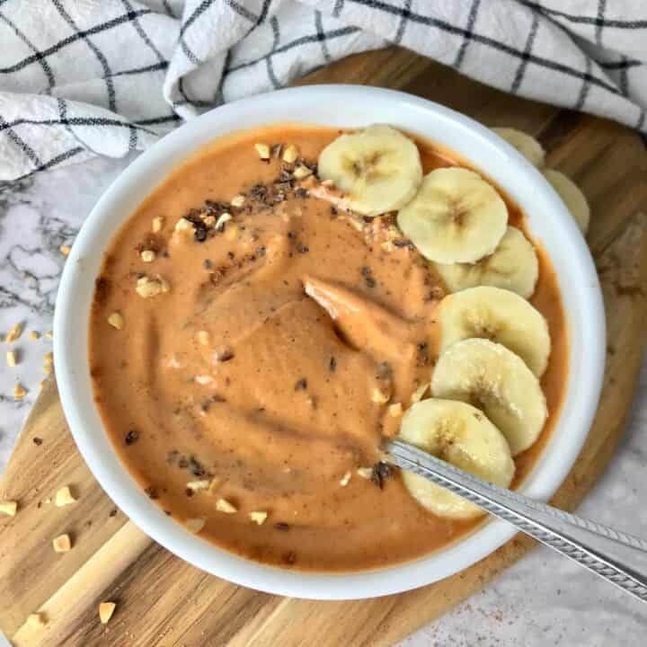 A bowl with a thick orange colored smoothie topped with banana slices.