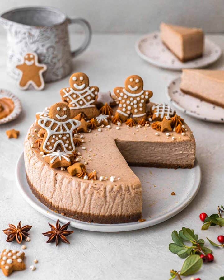 A cheesecake topped with gingerbread men with a two slices cut out.