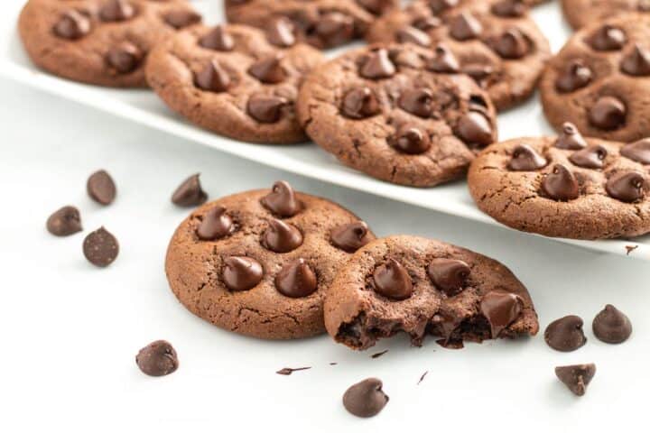 Chocolate cookies toped with chocolate chips on a white plate and surface.