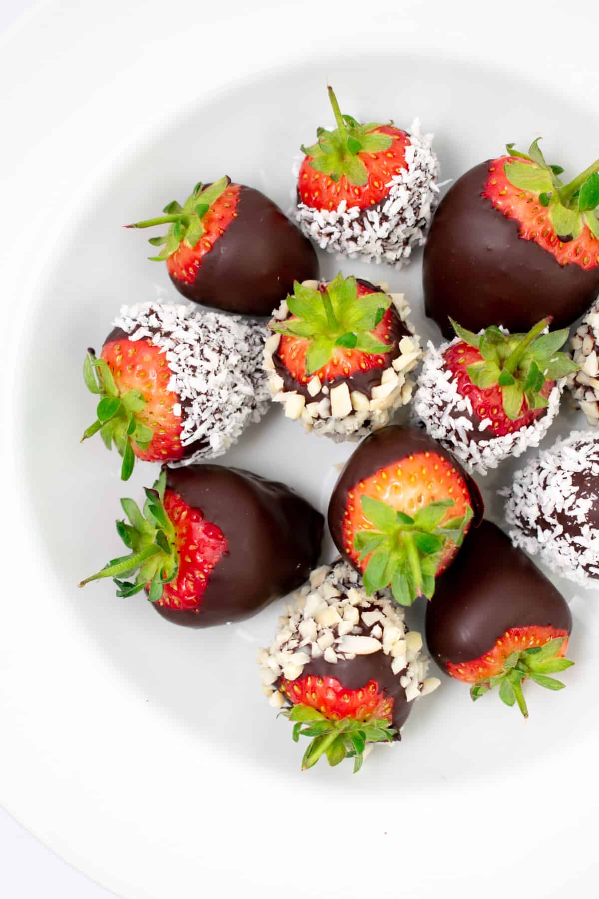 Strawberries covered in chocolate, coconut and almonds in a white bowl.