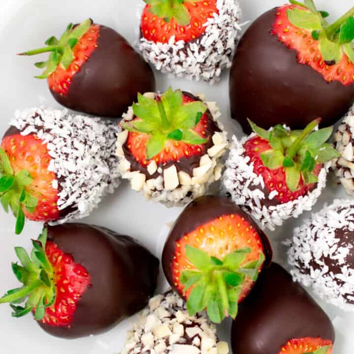 Strawberries covered in chocolate, coconut and almonds in a white bowl.