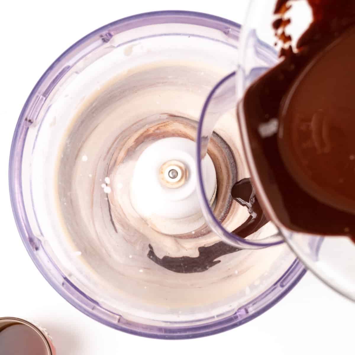 Pouring melted chocolate into a food processor with silken tofu in.