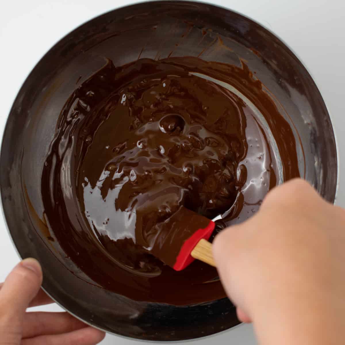 Stirring melting chocolate in a metal bowl.