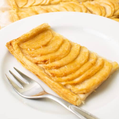 A slice of apple tart on a white plate with a fork.