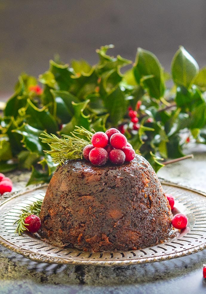 A Christmas pudding topped with cranberries, with holly behind it,
