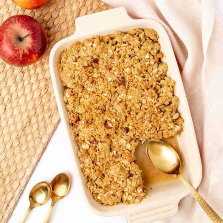Apple crisp in a baking dish with one portion removed.