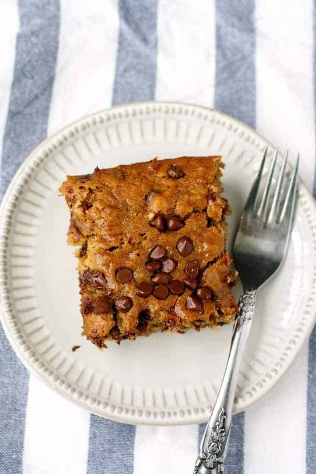 A square of banana cake with chocolate chips on a plate with a fork.