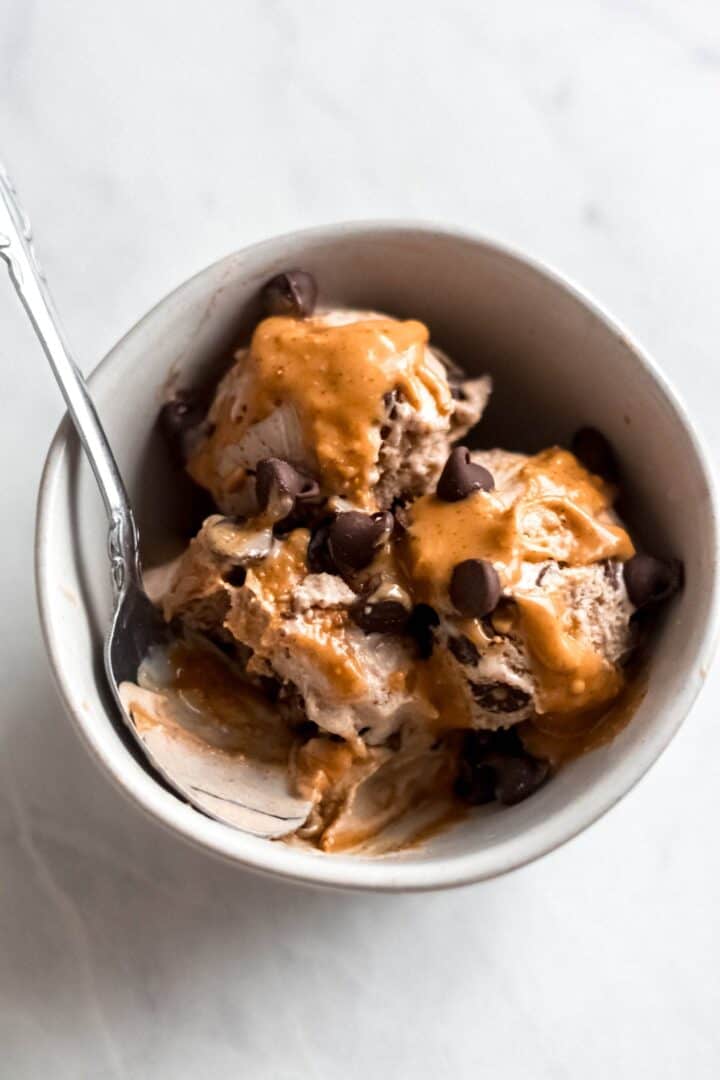 Ice cream topped with cramel sauce and chocolate chips in a bowl with a spoon.