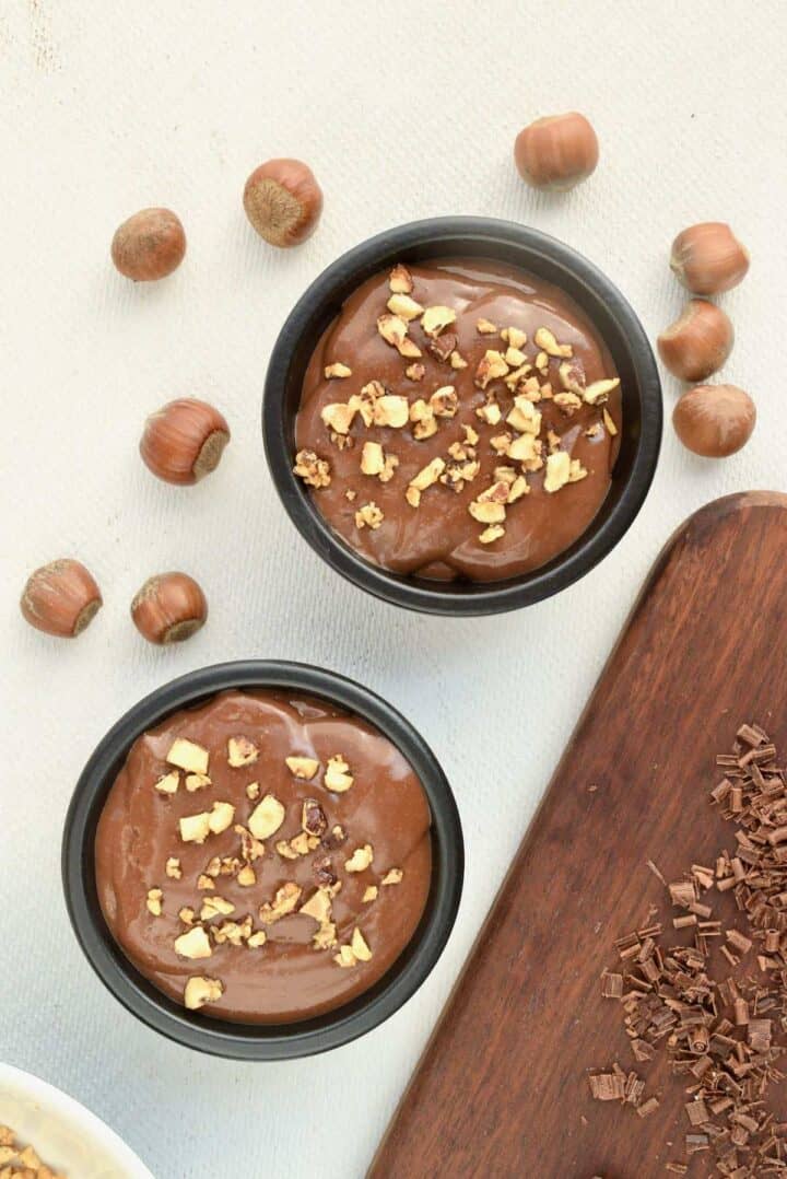 Two pots of chocolate pudding topped with hazelnut pieces.