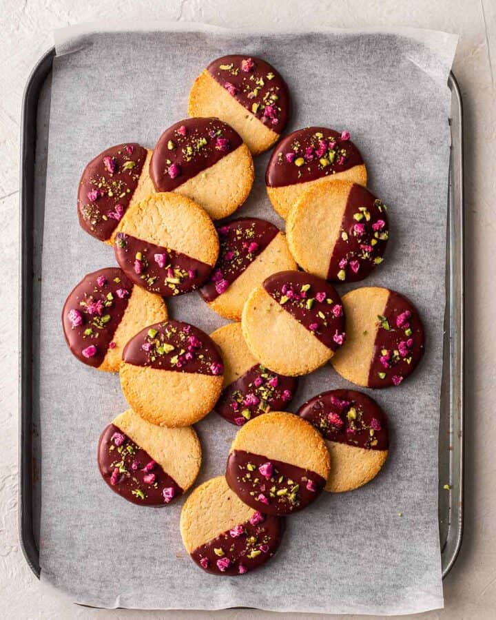 Round shortbread cookies half dipped in chocolate, pistachios and dried raspberries.