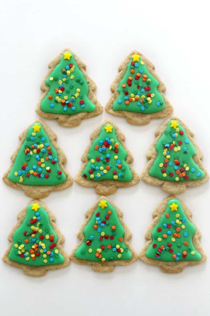 Eight Christmas tree shaped sugar cookies decorated with green icing and sprinkles.