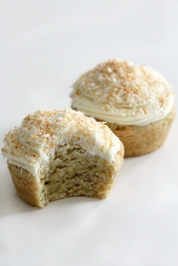 Two cupcakes decorated with shredded coconut and frosting.