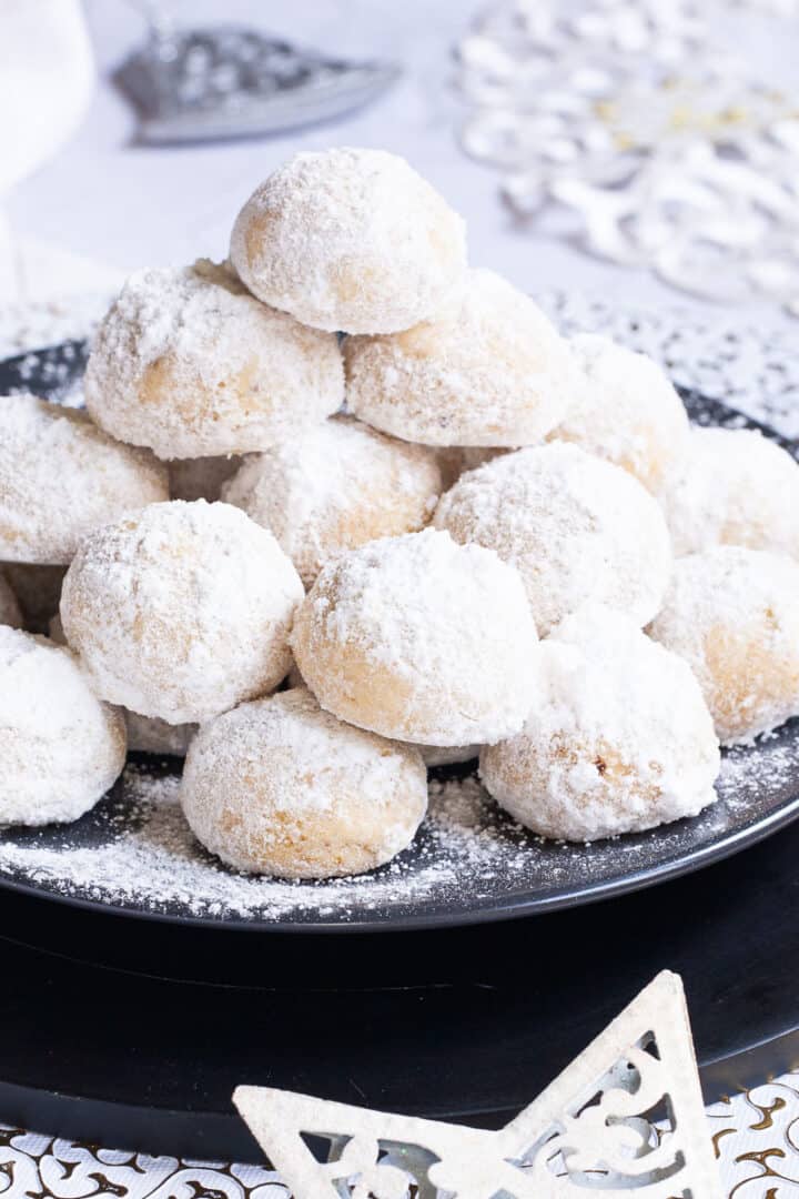 A stack of sugar-dusted ball-shaped cookies on a black plate.