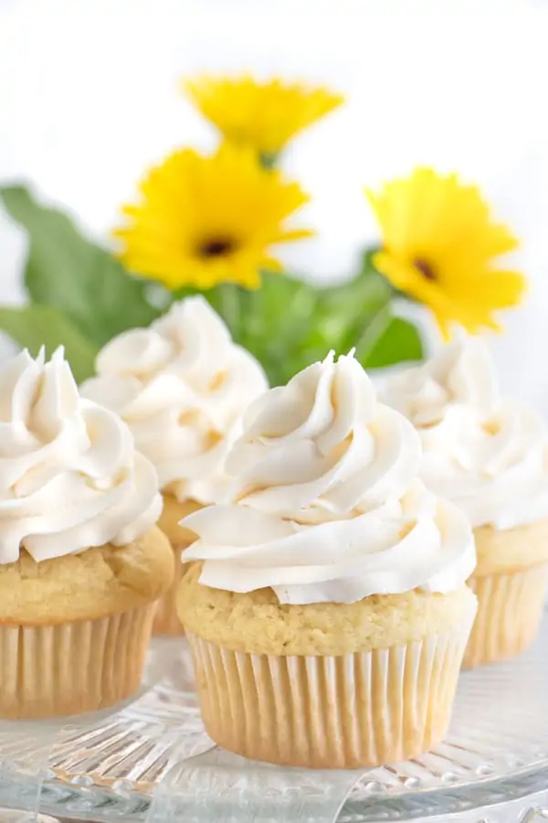 Cupcakes with vanilla buttercream on top, with yellow flowers in the background.