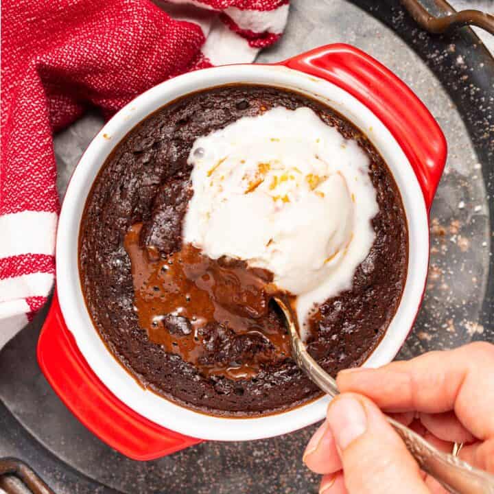 A spoon dips into a chocolate lave cake topped with ice cream.