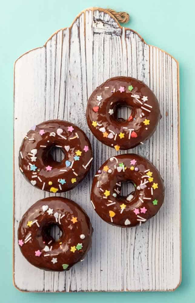 Four chocolate and sprinkle covered donuts on a wooden board.