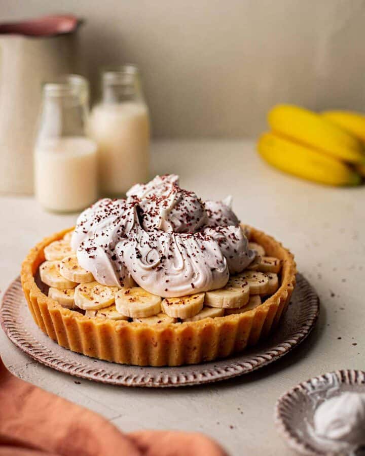 A pie with sliced bananas and a pile of whipped cream on top.