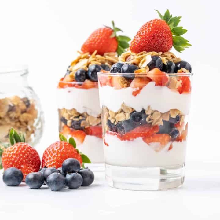 Two glasses layered with yogurt, granola and berries.