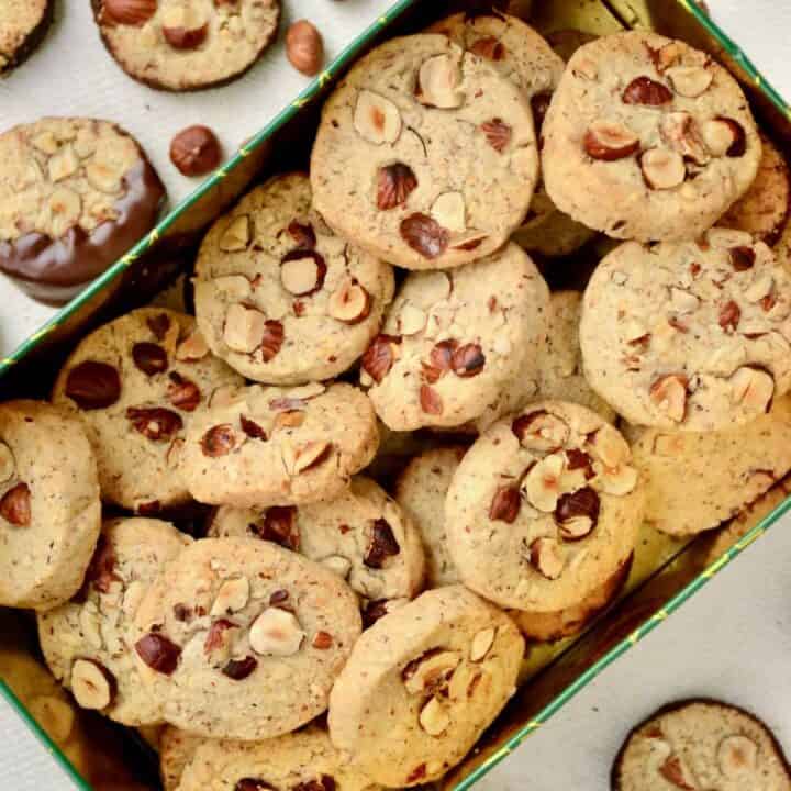 Small cookies topped with hazelnuts in a rectangular tin.