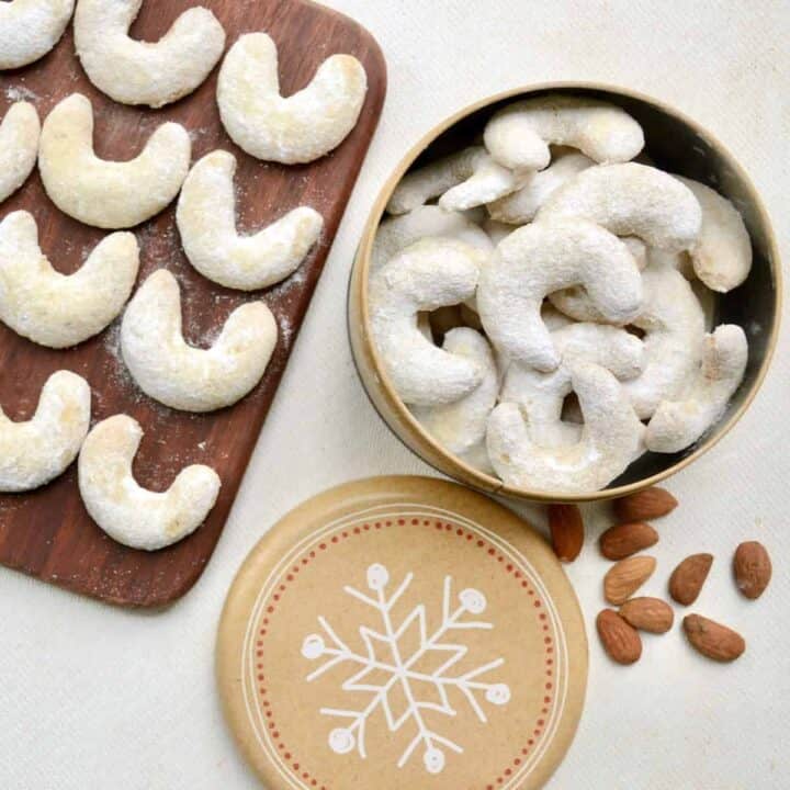 A tin full of crescent shaped cookies topped in icing sugar.