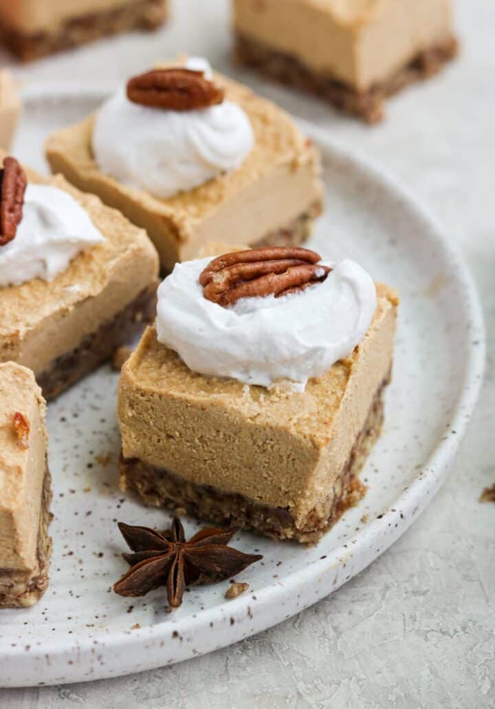 Squares of pumpkin cheesecake topped with whipped cream and a pecan.