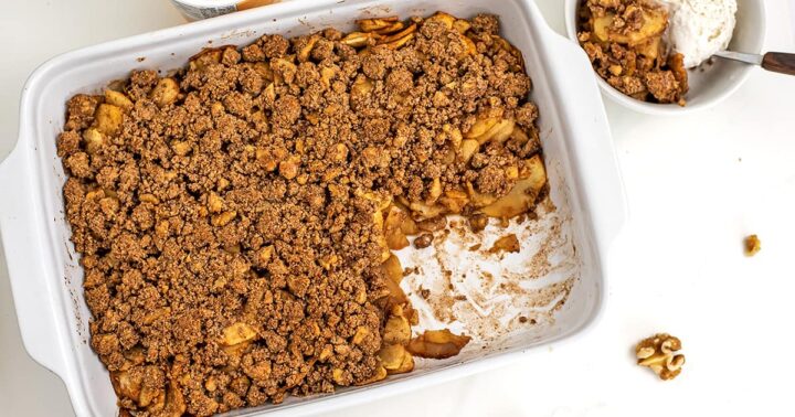 A baking dish with apple crumble and a portion already served in a bowl.