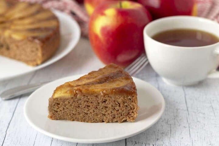 A slice of apple topped cake next to a cup of tea.
