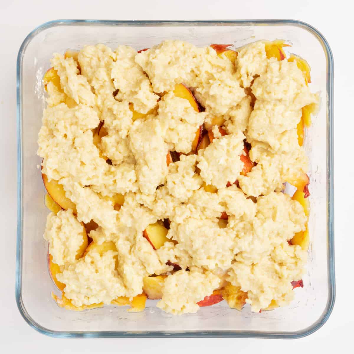 Pieces of cobbler topping spread on top of peaches in a baking dish.
