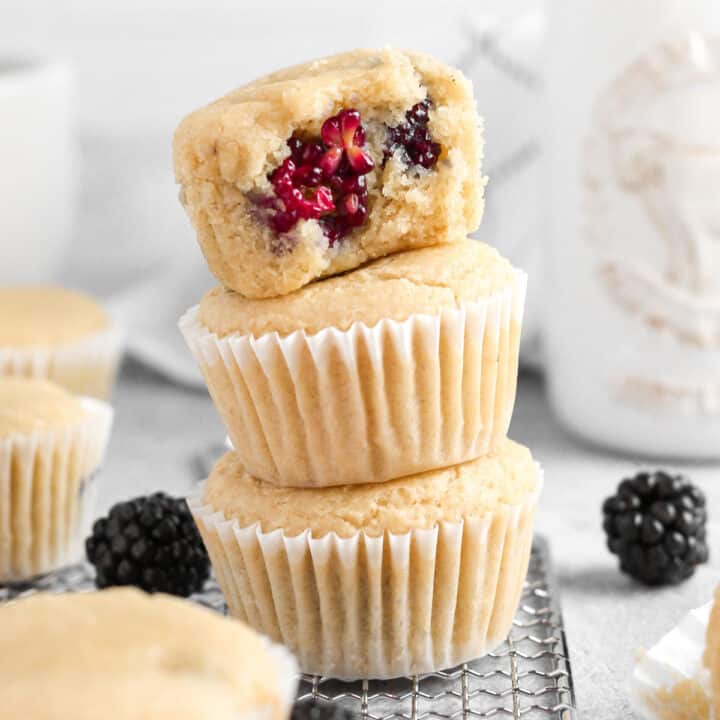 A stack of three muffins, the top one is open revealing blackberries inside.