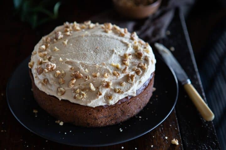 A frosted carrot cake on a dark plate.