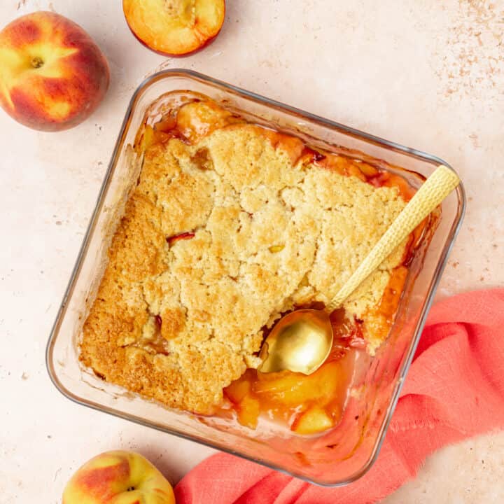 Vegan peach cobbler in a baking dish, with a portion already served.
