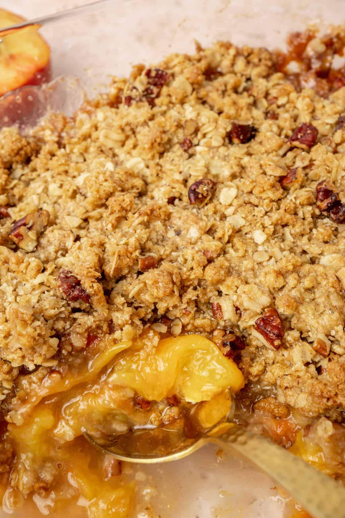 A spoon digs into the juicy filling of a peach crisp.