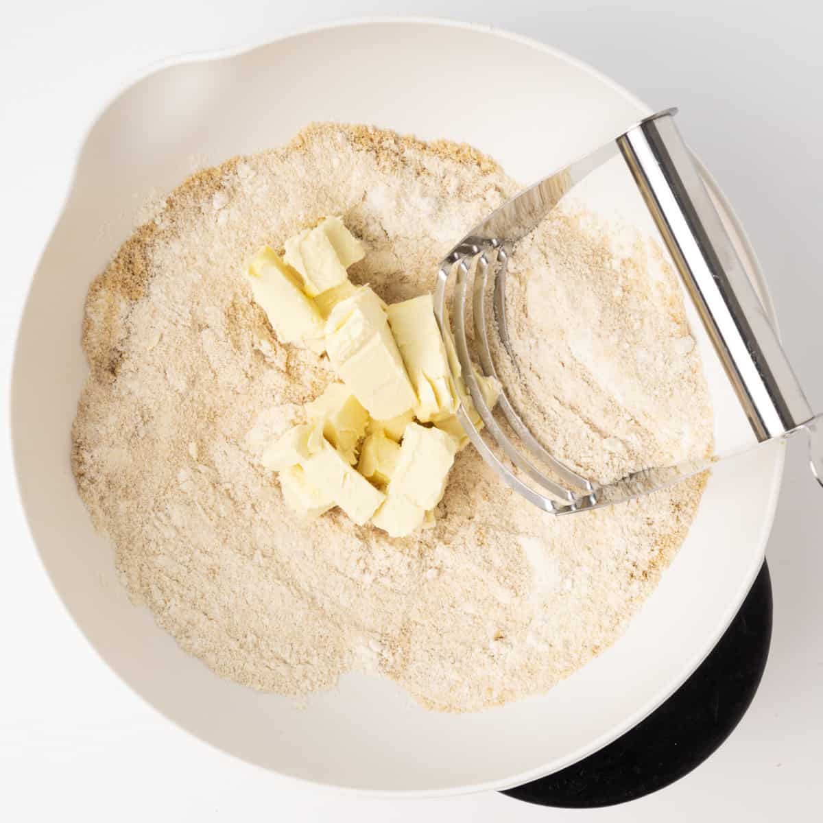Ctuiing butter into flour and sugar in a mixing bowl.