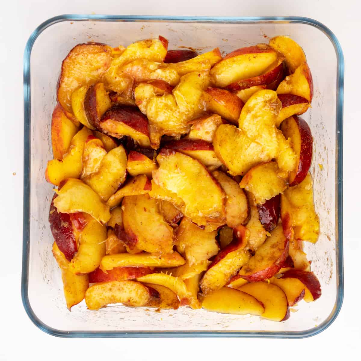 Sliced peaches mixed with spices, cornstarch and lemon in a baking dish.
