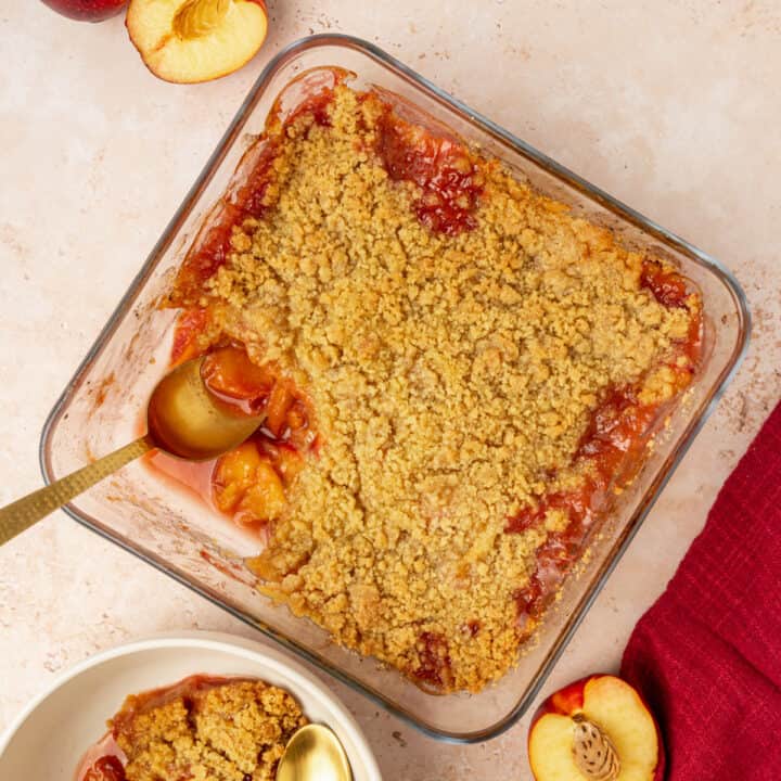 A peach crumble with a portion removed and a serving spoon.