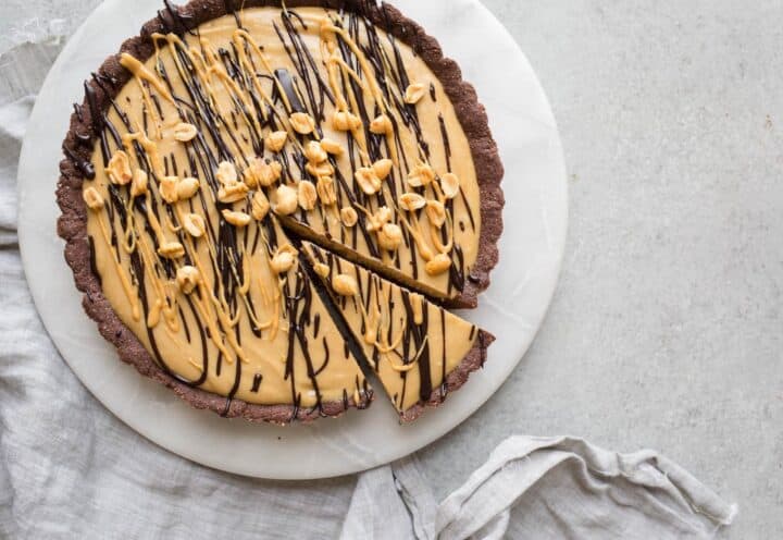 A peanut butter pie with chocolcate crust topped with nuts and sauce.