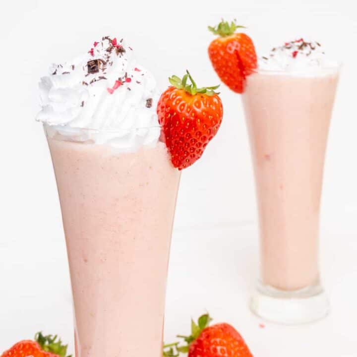 Two tall glasses of strawberry milkshake.