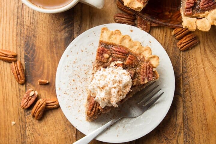 A slice of pecan pie topped with whipped cream on a plate.