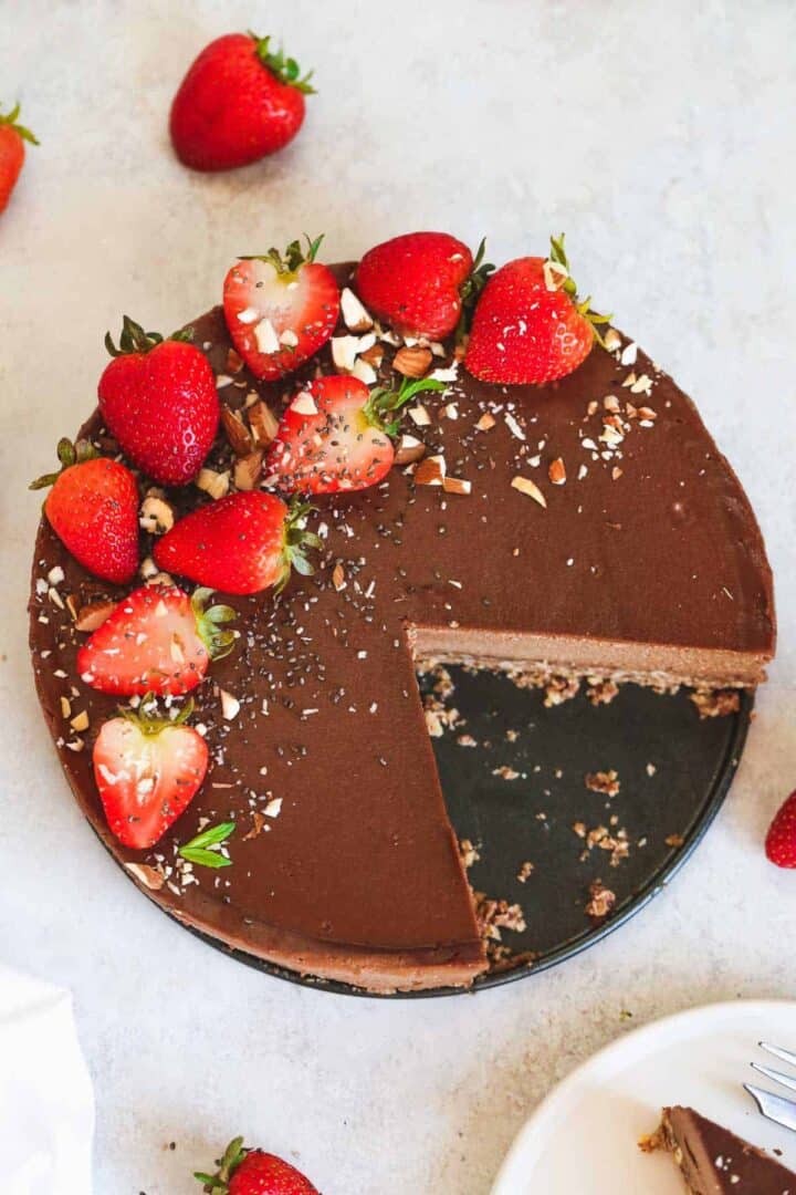 A chocolate cheese cake topped with strawberries with a slice missing.