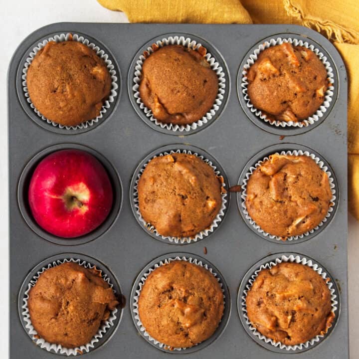 8 muffins and and one apple in a muffin tray.