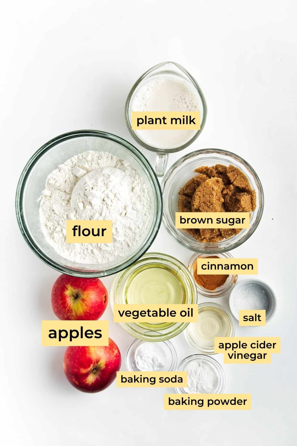 Ingredients for vegan apple muffins: All-purpose flour, brown sugar, apples, plant milk, vegetable oil, cinnamon, baking powder, baking soda, apple cider vinegar, and salt.