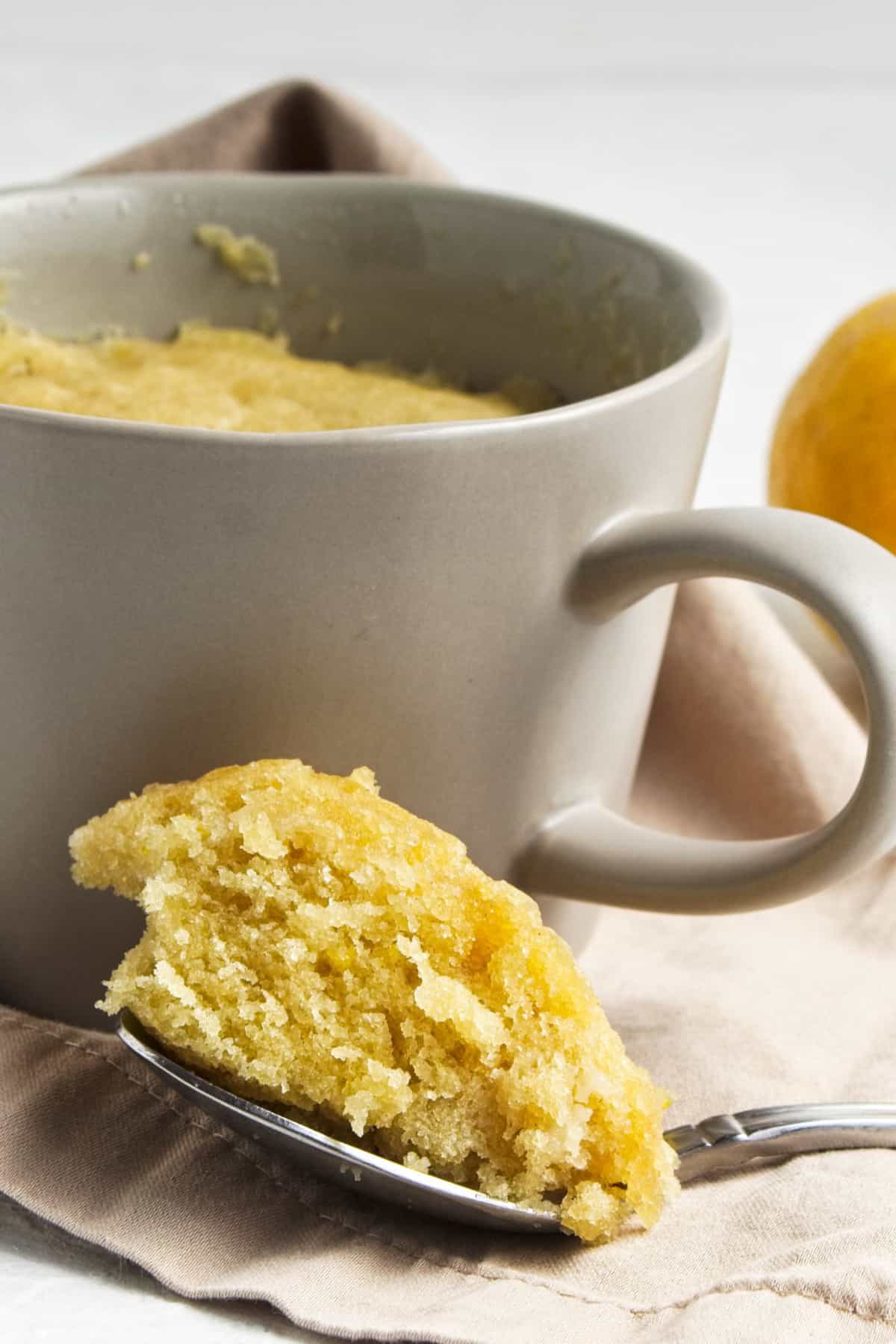 A spoonful of fluffy lemon cake next to a mug.