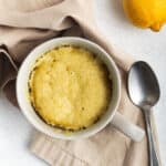Lemon mug cake on a napkin next to a spoon and lemon.