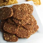 A pile of walnut shortbread cookies on a plate next to a yellow napkin.